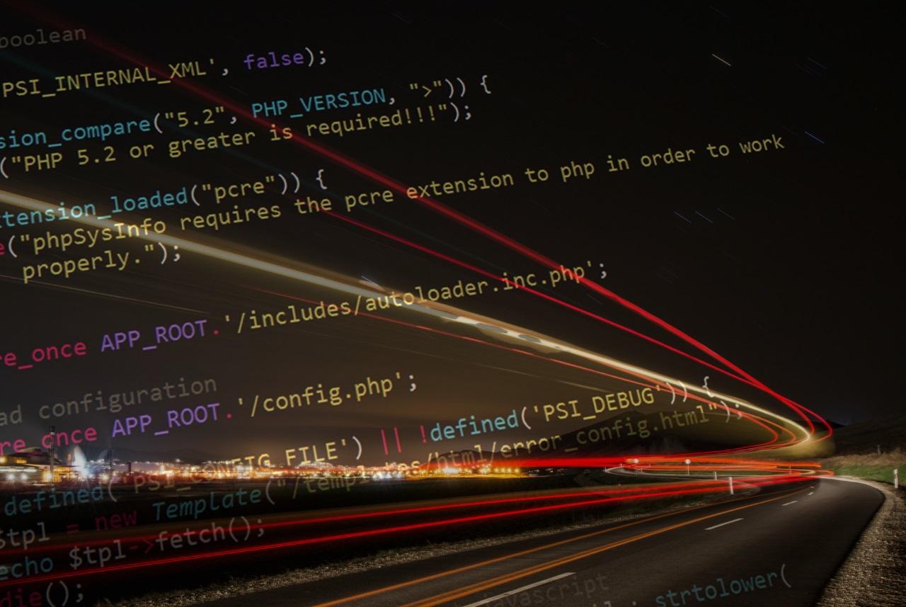 Lines of code overlaid on a night scene with light trails from moving vehicles on a curved road.